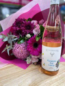 Image of a bottle of Flowers for Lucy Moscato with a bunch of bright pink coloured flowers in the background