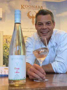 Image of Dru with a glass of Lucy & Alice Pinot Gris beside a bottle of it.