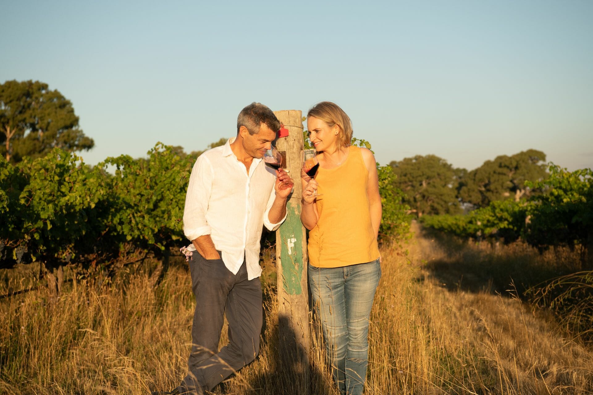 Dru & Nicole Reschke holding a Koonara Wines glass in an organic vineyard.