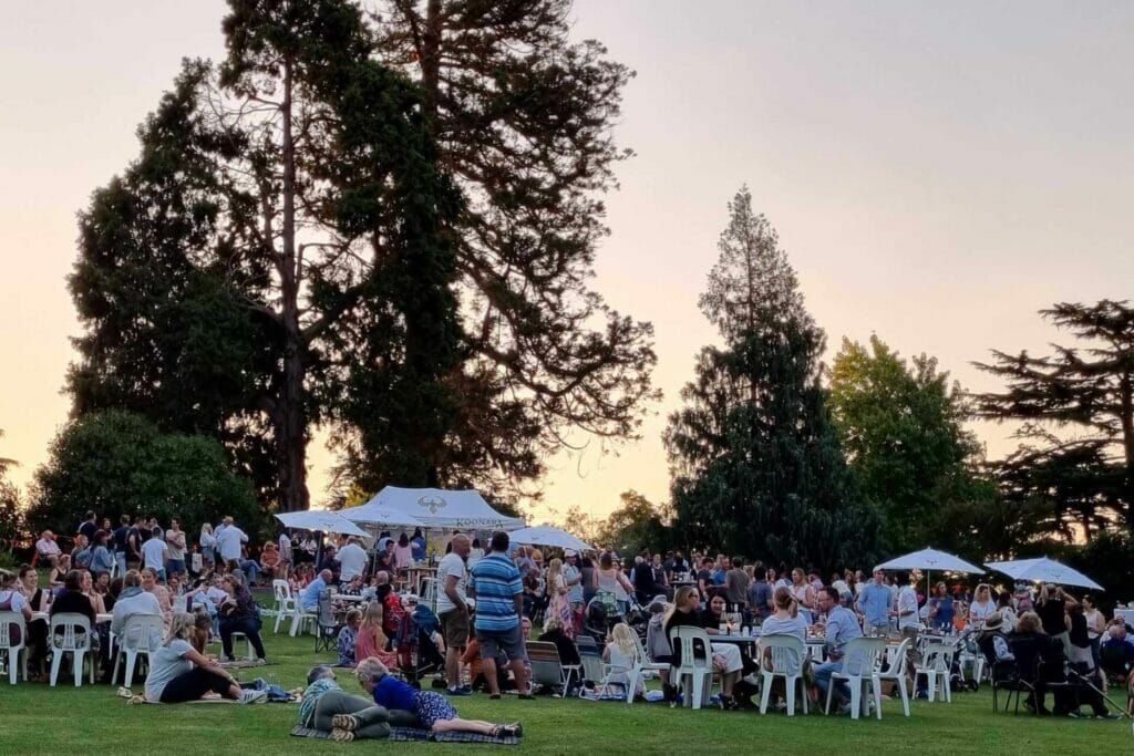 A crowd of people in the Hamilton Botanic Gardens at the pop up festival right on Dusk with Koonara Tents and trees in the background