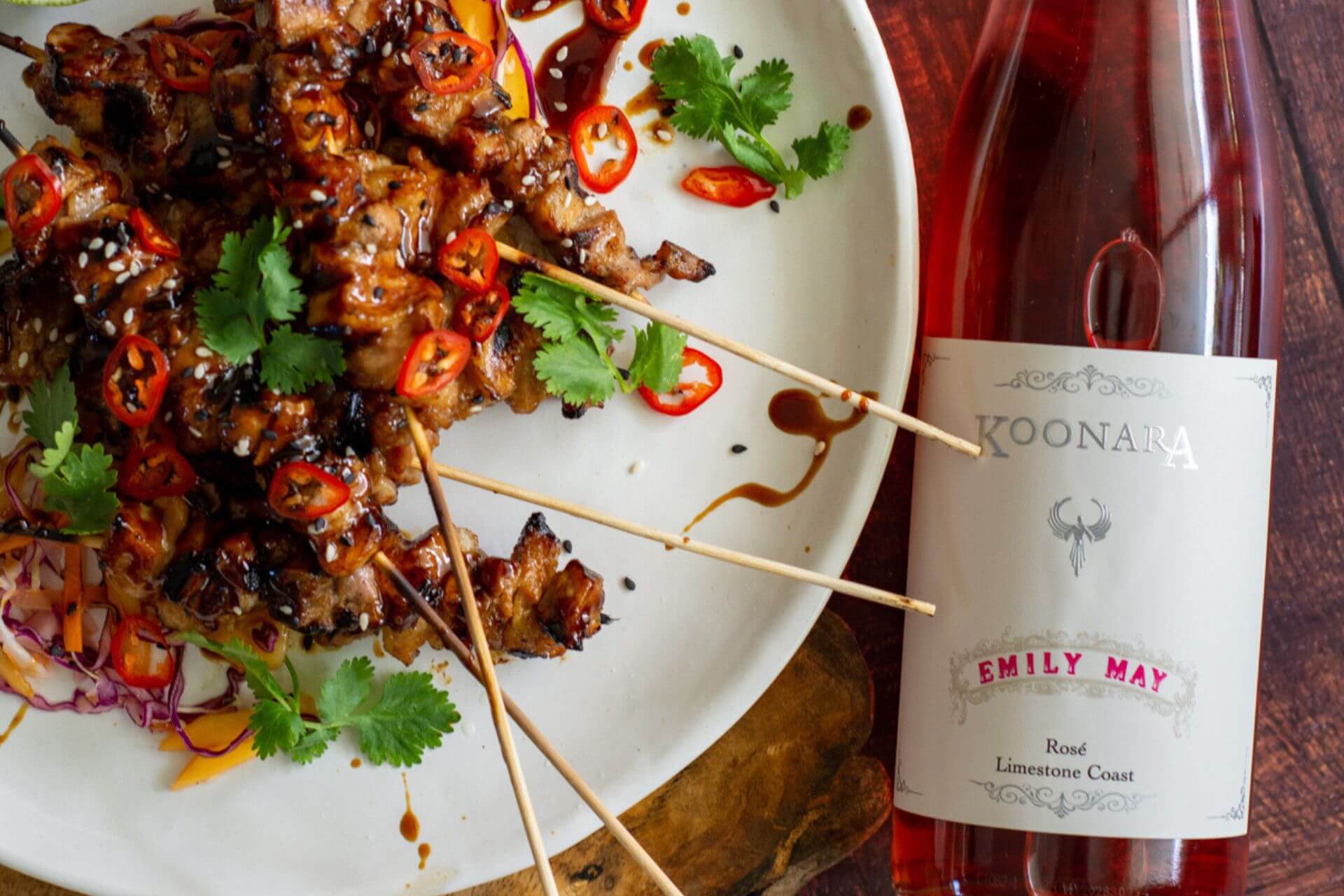 The Pork belly Skewers on a plate with a bottle of Email May Rose alongside it since they pair so well together