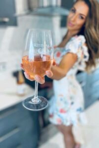 A glass of Moscato being held by a woman who is blurry in the background the glass of wine is sharply in focus.
